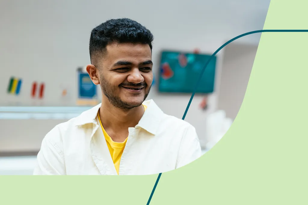 A young man with a beard, wearing a yellow T-shirt and white shirt, smiles warmly, showcasing the welcoming environment for interns at Aviva.