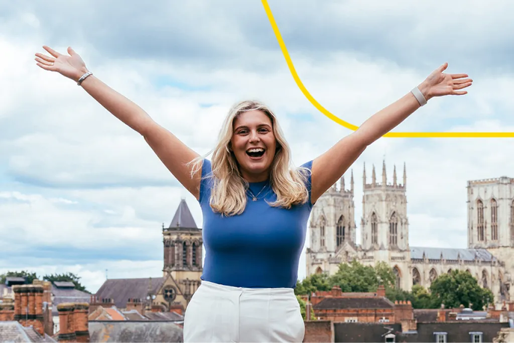 Young blonde woman smiles brightly with arms spread wide, exuding confidence and enthusiasm, ready to embrace new opportunities at Aviva.