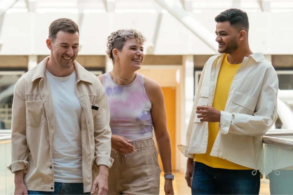 Three young people casually dressed - two men in jeans and T-shirts and a woman in shorts - walk through a modern office building, embodying the dynamic and inclusive nature of Aviva’s apprenticeship opportunities. 